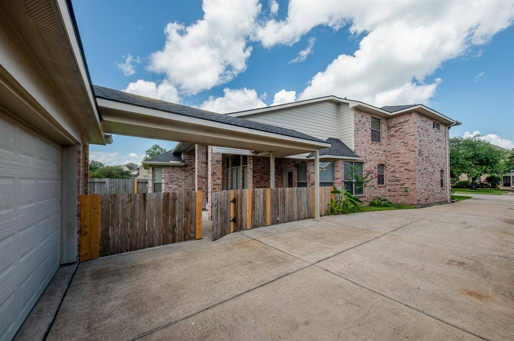 This photo shows a spacious two-story brick home with a large driveway and attached garage. The property features a covered entryway and a wooden fence, providing a sense of privacy and ample parking space. The home is set in a suburban neighborhood in desirable Katy, TX.
