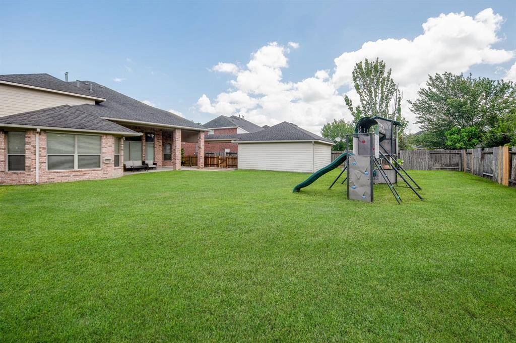 Spacious backyard with a well-maintained lawn, a playset for kids, and a covered patio area perfect for outdoor entertaining. The yard is fenced for privacy.