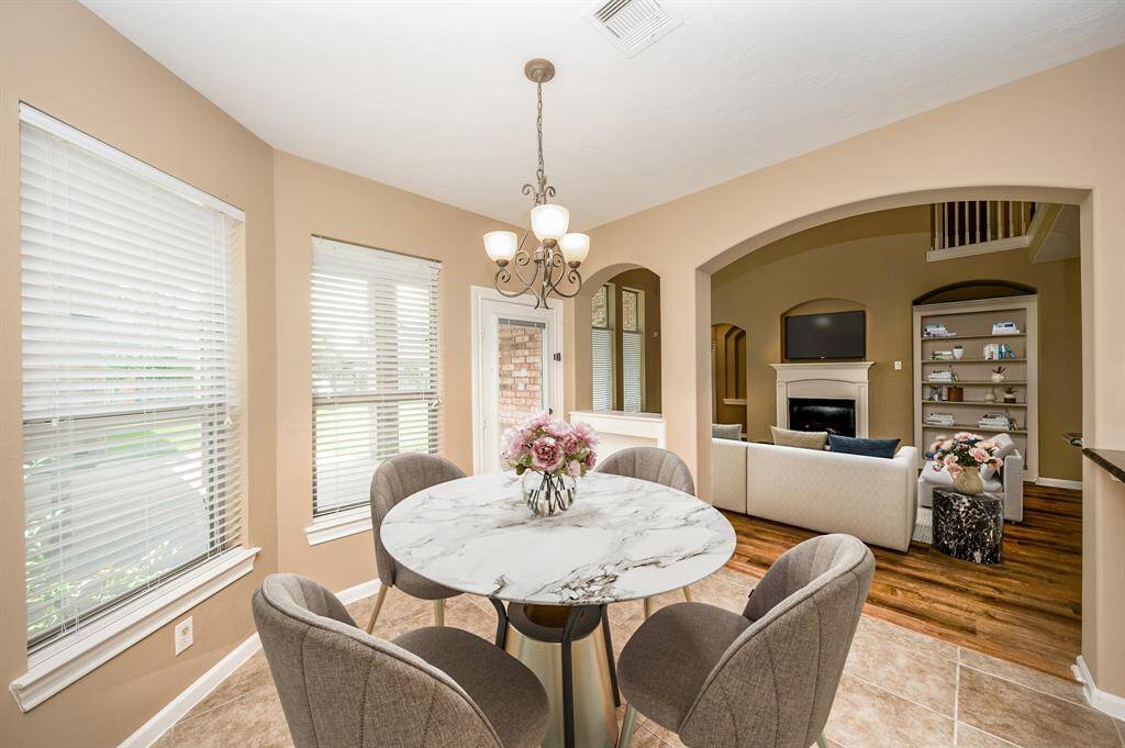 This photo showcases a bright, open-concept dining area with large windows. The space seamlessly connects to a cozy living room featuring a fireplace and elegant decor, ideal for entertaining or family gatherings. Image is Virtually Staged.