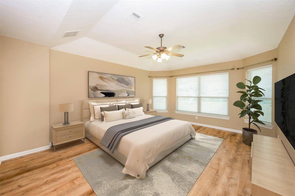 This spacious primary bedroom features warm neutral tones, large windows providing ample natural light. It includes a ceiling fan, beautiful  floors. Image is Virtually Staged.