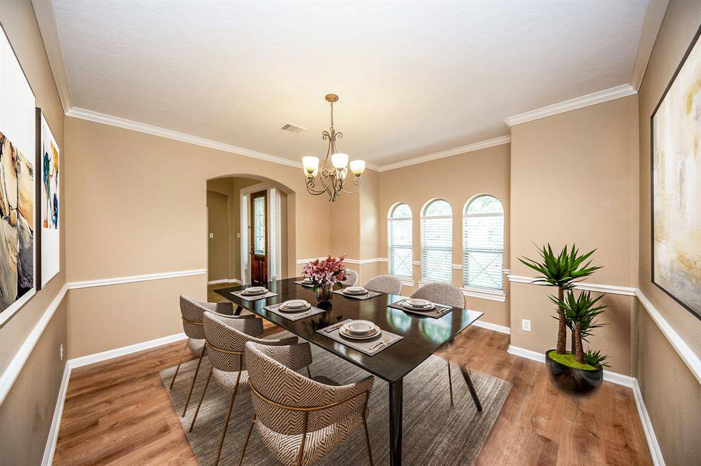 This dining room features warm beige walls and elegant lighting. It has three arched windows allowing plenty of natural light for a welcoming atmosphere.   Image is Virtually Staged.