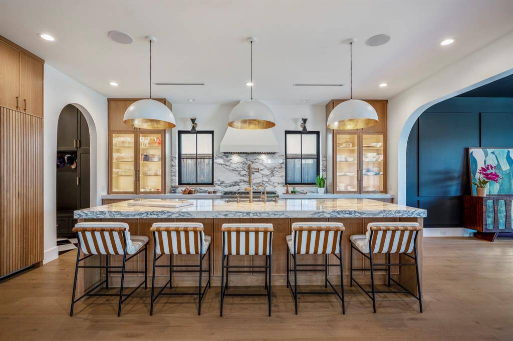 An incredible chef's island made of three-inch Arabescato Corchia polished marble. Seats five people comfortably under ambient pendant lighting. Island includes storage space.