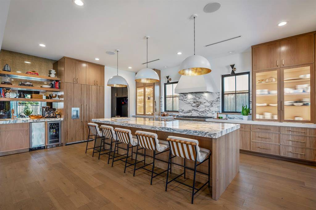 At the bar to the left, Hoshizaki Top Hat Cuber Icemaker, air-cooled with built-in storage along with a Titan Signature 48-can beverage fridge. Custom reeded wood-paneled built-in Gaggenau fridge.