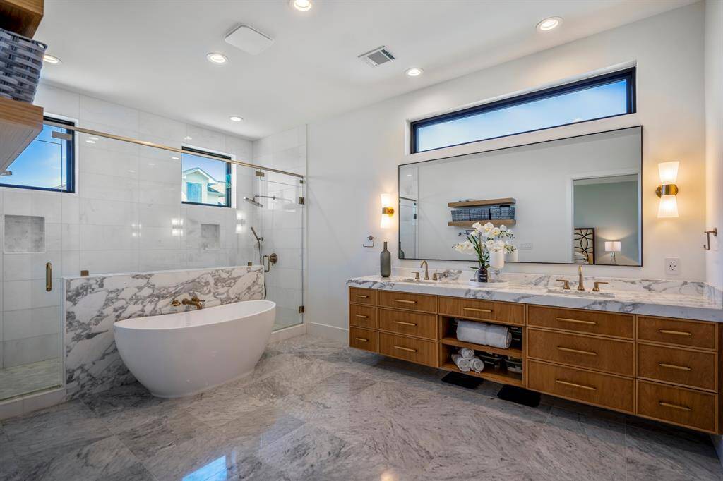 Showcased is a slab of Arabescato Vagli marble behind a modern soaking tub. Delta hardware, and Grecian Thassos white marble tiles line the shower under privacy windows.