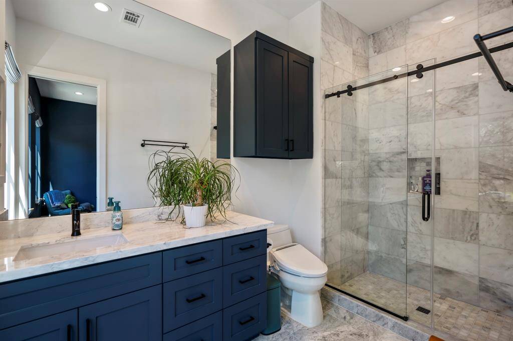 This en-suite bathroom features a Kohler toilet, marble counters, and a beautiful walk-in shower.