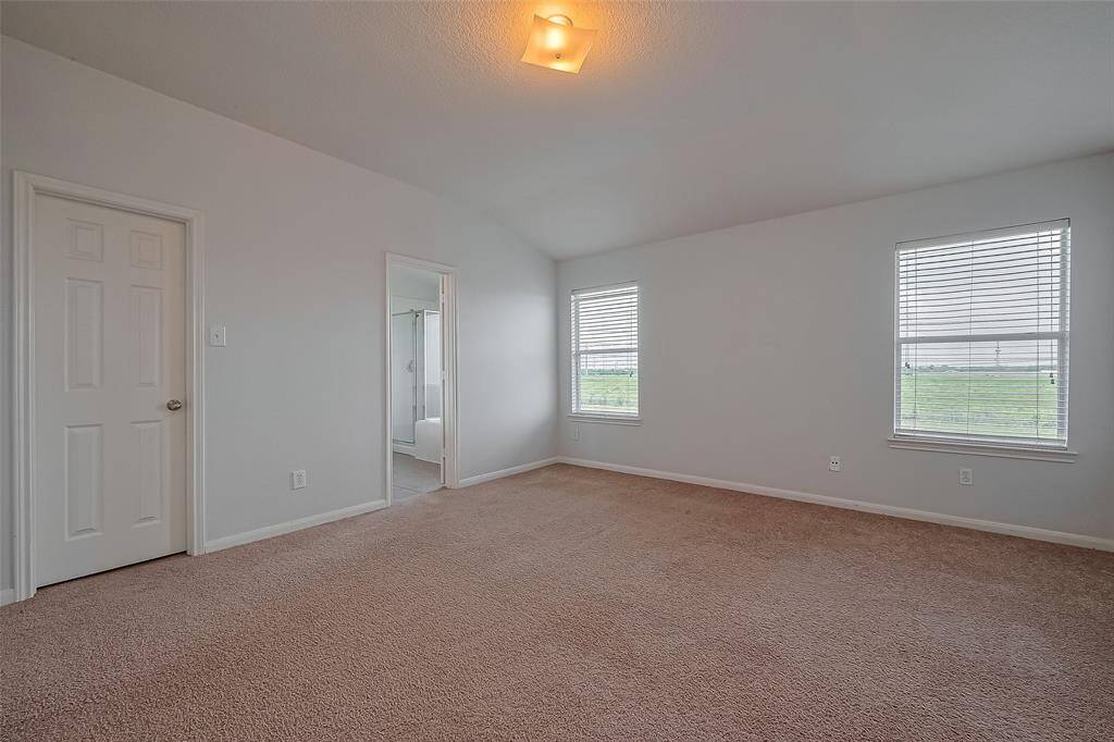 This spacious primary bedroom features neutral walls, two large windows providing ample natural light, a ceiling light fixture, and an en-suite bathroom for convenience.
