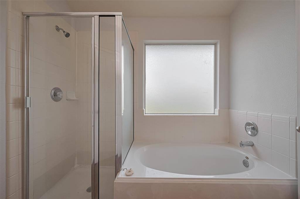 This primary bathroom features a sleek glass-enclosed shower and a spacious bathtub, complemented by a frosted window for privacy and natural light.