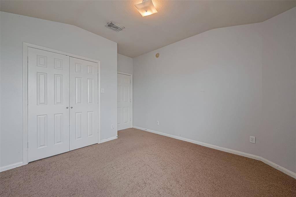 This is a clean, neutral-colored room featuring carpeted flooring, a small ceiling light, and a closet with double doors, ideal for a bedroom or office space.