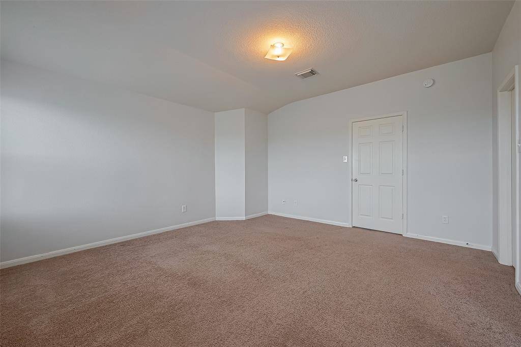 Spacious, carpeted room with neutral walls, a ceiling light, and a white door, ideal for a bedroom or office setup.