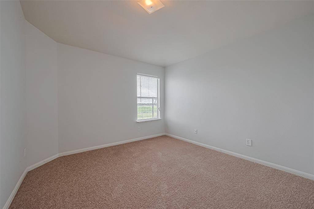 This room features neutral-colored walls and carpet, a single window for natural light, and a ceiling light fixture, offering a simple and versatile space.