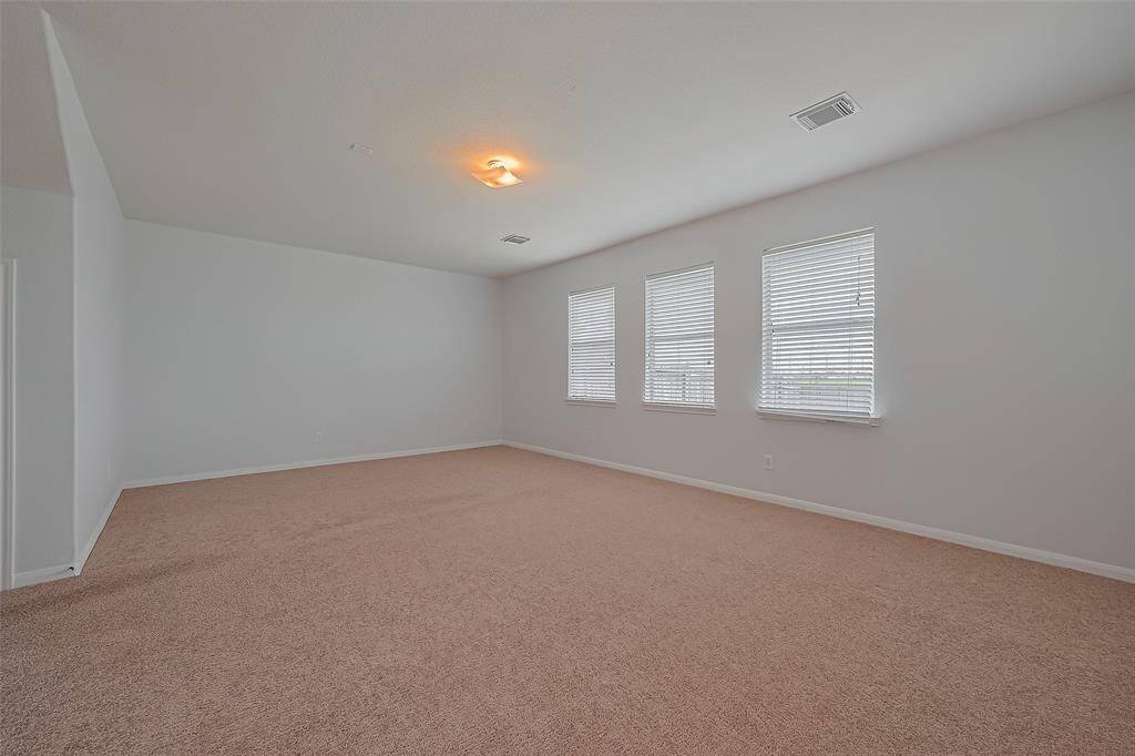 This spacious living room features neutral walls and ample natural light from three large windows, making it ideal for a versatile living area.