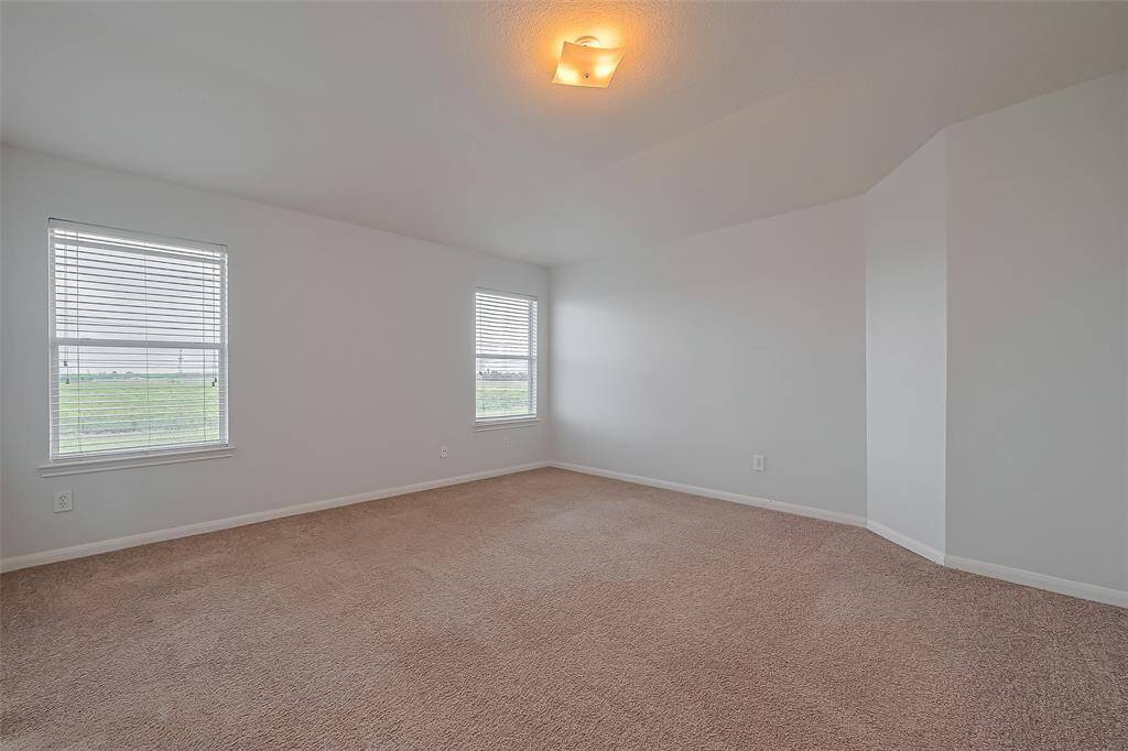Upstairs primary bedroom features neutral carpeting and walls, creating a blank canvas for personalization. It has two large windows that let in plenty of natural light, offering serene views of the surrounding landscape.