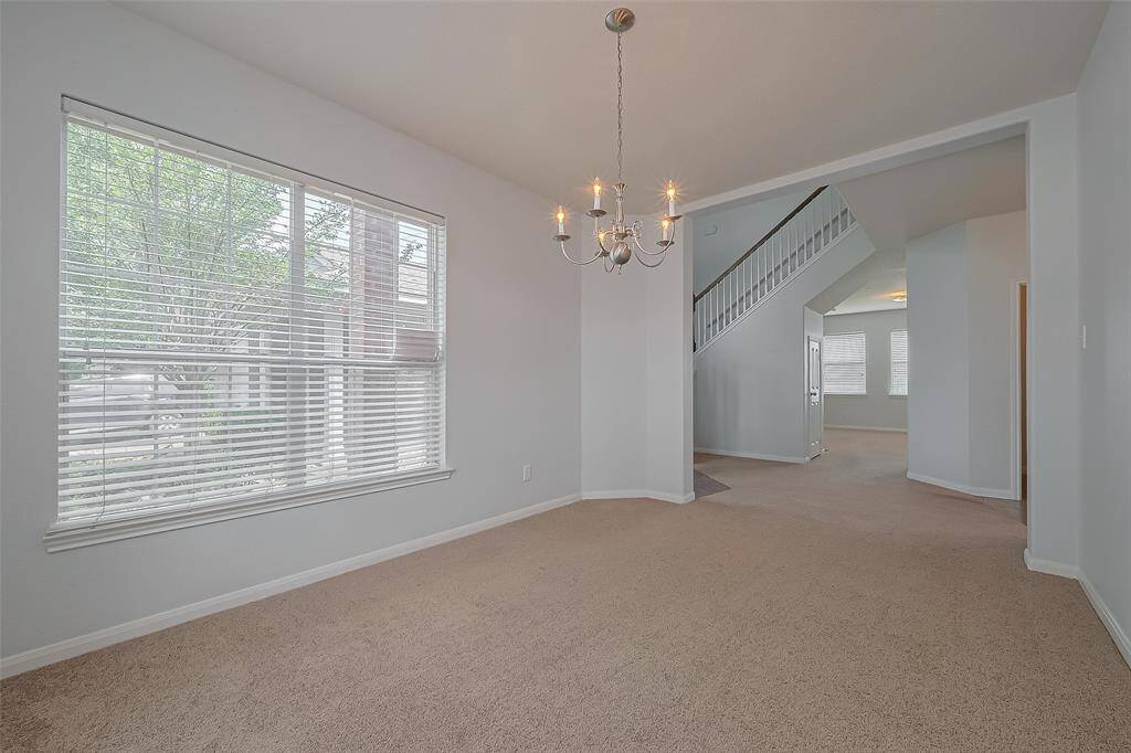 Bright dining room with neutral walls, featuring a large window with blinds and a chandelier.
