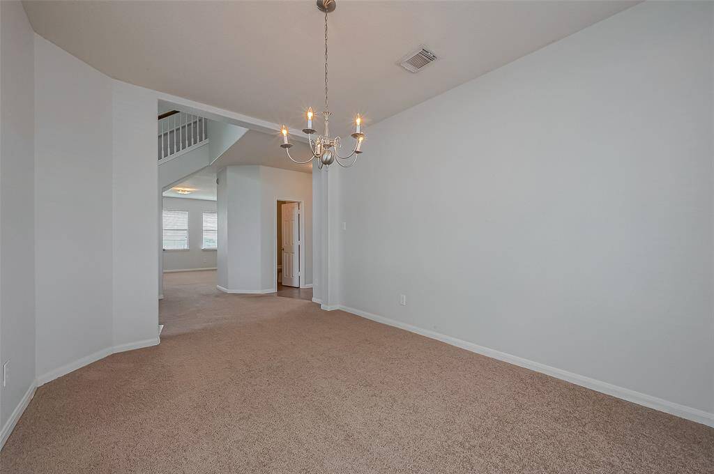 This photo showcases a spacious, carpeted dining area with a modern chandelier. The room leads into a bright living space with large windows, and has access to a staircase with a partial view of an upstairs area.