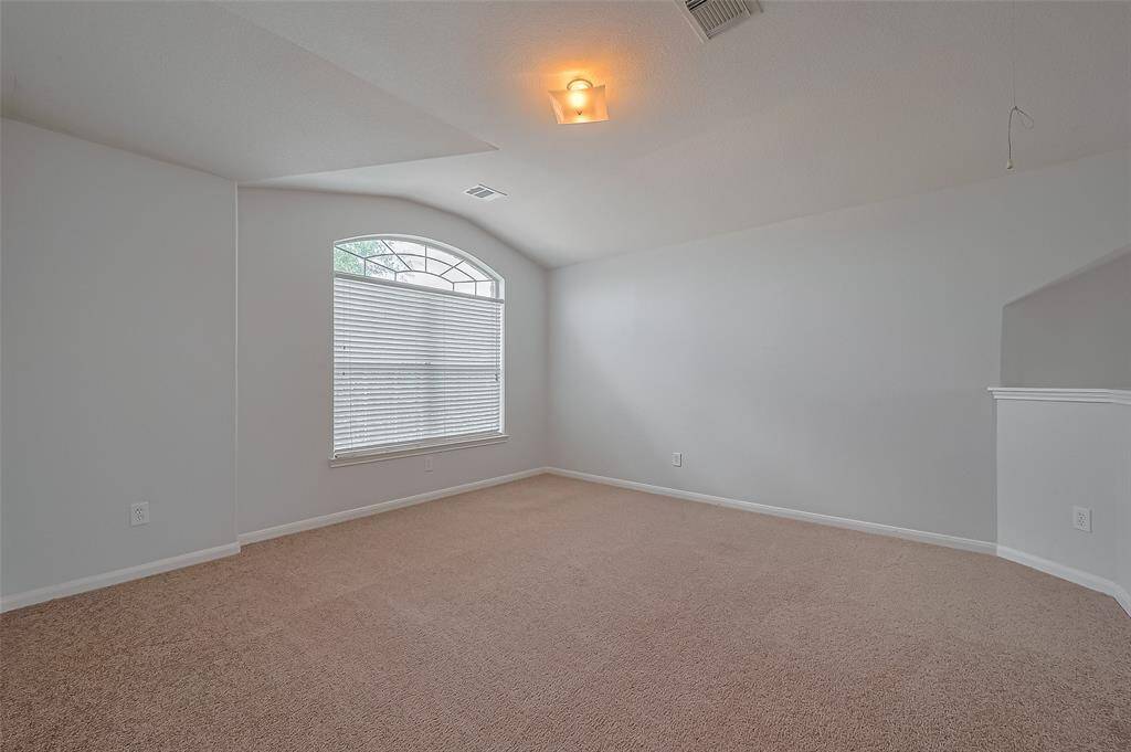 This room features neutral walls, a soft carpet, and a large window with blinds, offering natural light. The ceiling is slightly vaulted, adding spaciousness, and there's a simple ceiling light fixture.