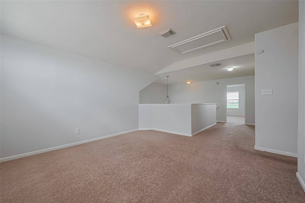 This room features a spacious, carpeted open area with neutral walls and ceiling lights. It includes a partially enclosed section, ideal for a small office or sitting area, and a visible adjacent room. Perfect for versatile use and personal customization.