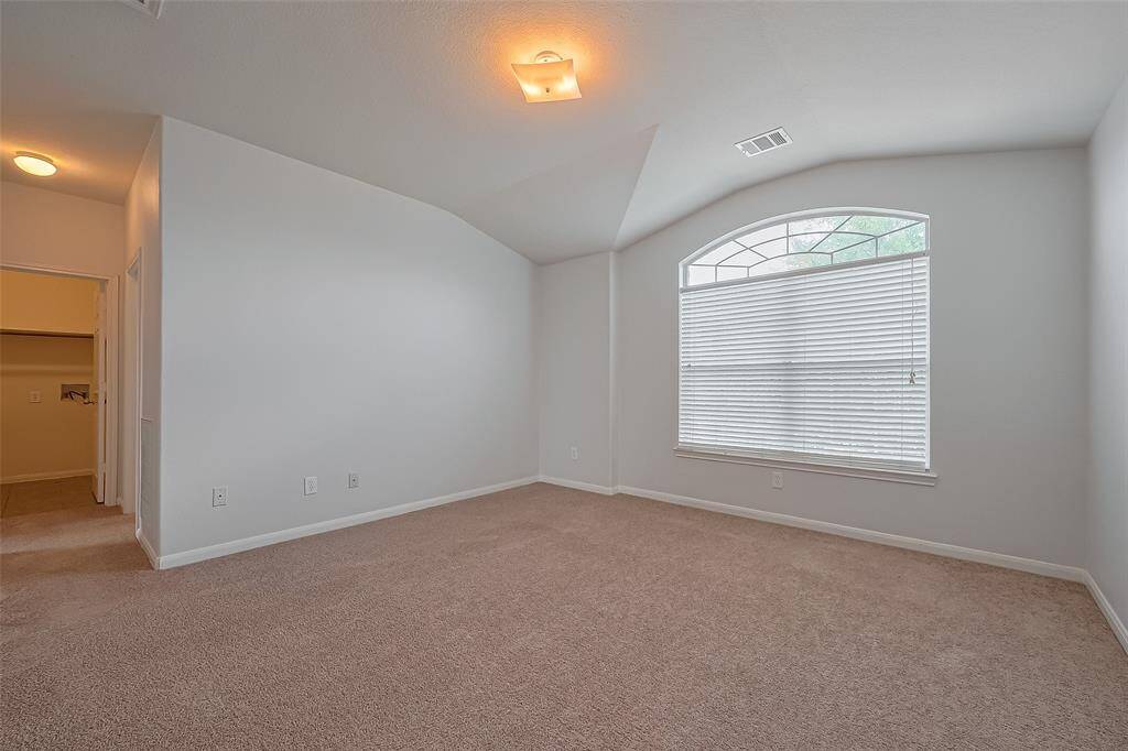 This room features a spacious layout with neutral walls and carpet, a large arched window providing natural light, and a ceiling light fixture. There's a doorway leading to additional space, possibly a closet or bathroom.