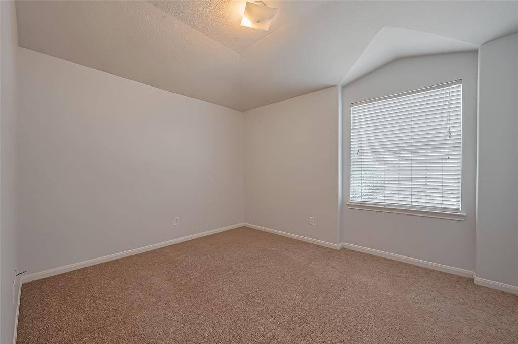 This photo shows a cozy, carpeted room with neutral walls, a ceiling light, and a large window with blinds, providing natural light. Perfect for a bedroom or home office.