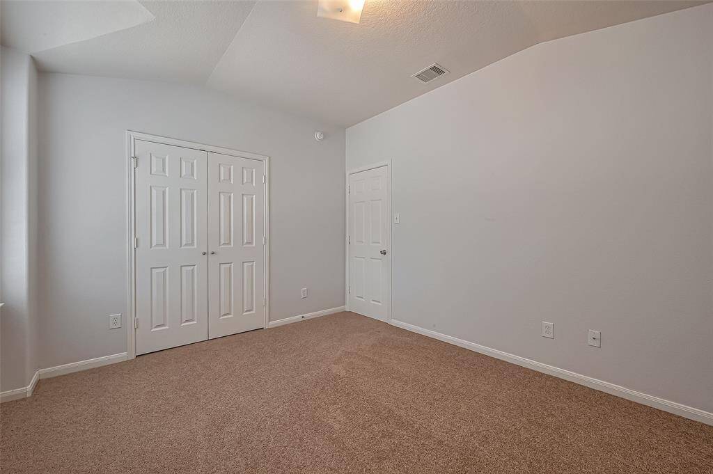 Bright, spacious bedroom with neutral carpet and walls, featuring a double closet and ample natural light. Ideal for a cozy, personalized space.