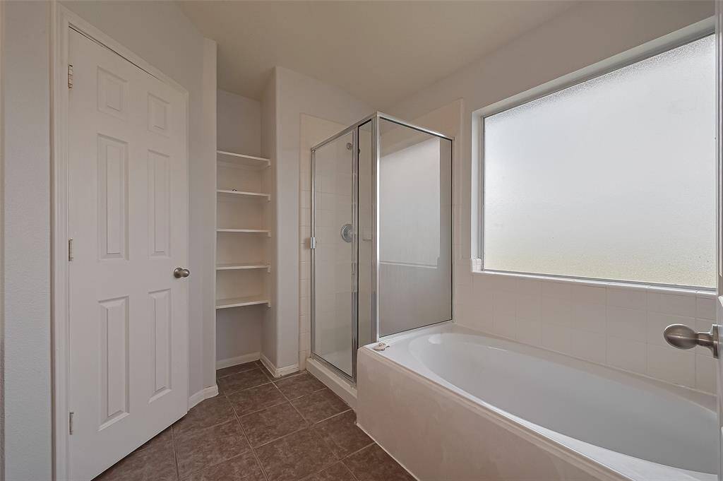 The bathroom features a clean, modern design with a spacious bathtub, glass-enclosed shower, built-in shelving, and a large frosted window for natural light.