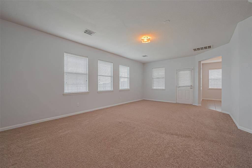 This spacious living room features ample natural light from several windows overlooking backyard. The open layout connects to kitchen and breakfast area. Door leads to covered patio.