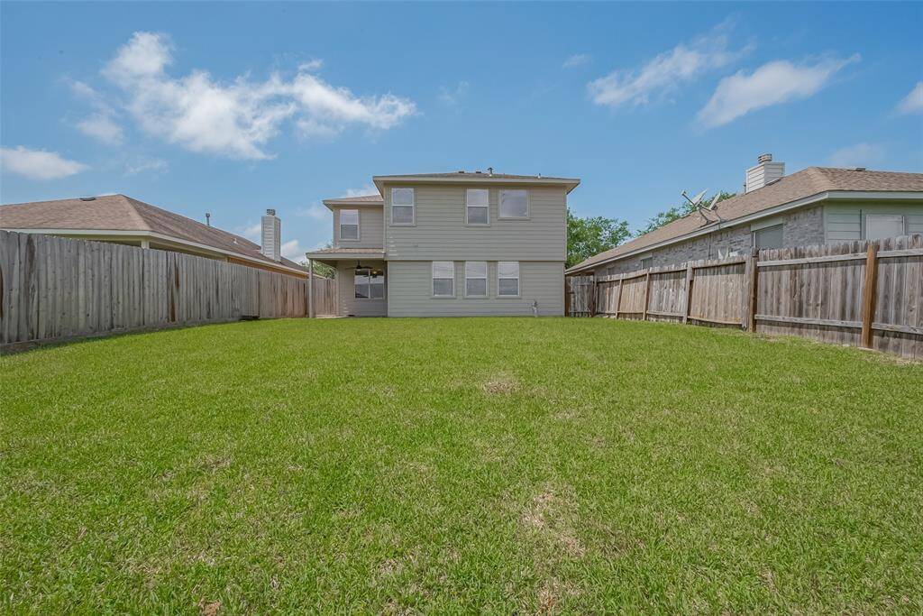 Spacious backyard with a well-maintained lawn, enclosed by wooden fencing. The house is a two-story structure with light-colored siding, offering a private and serene outdoor space.