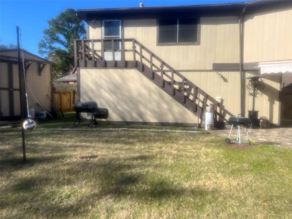 This photo shows a two-story house with beige siding and brown trim. It features an external staircase leading to an upper deck. The yard includes a grill and patio area.