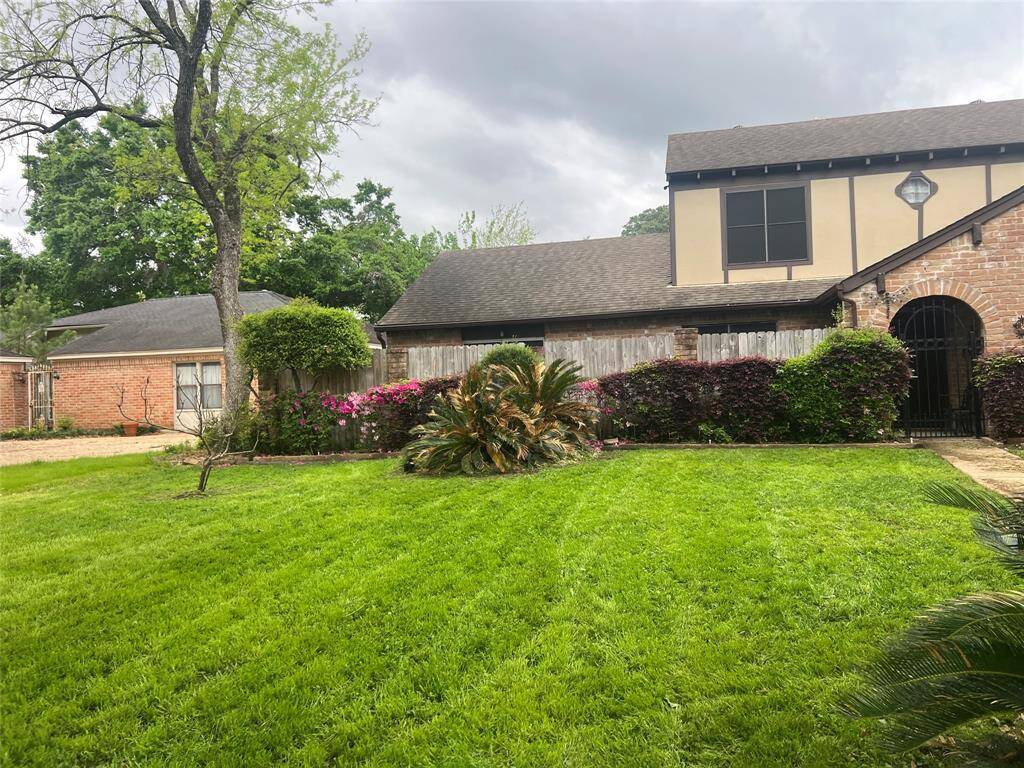 Charming two-story home with a well-maintained lawn, mature trees, and vibrant shrubs. The brick exterior and gated entry add character and privacy. Great curb appeal in a lush, green setting.
