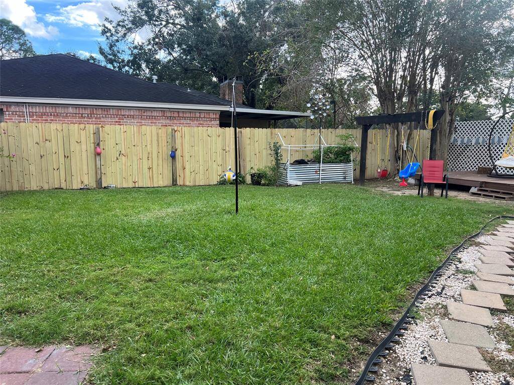 This backyard features a well-maintained lawn, a wooden fence for privacy, and a small deck area. There's a pergola with seating and a garden bed for planting. A playful swing set adds a family-friendly touch.