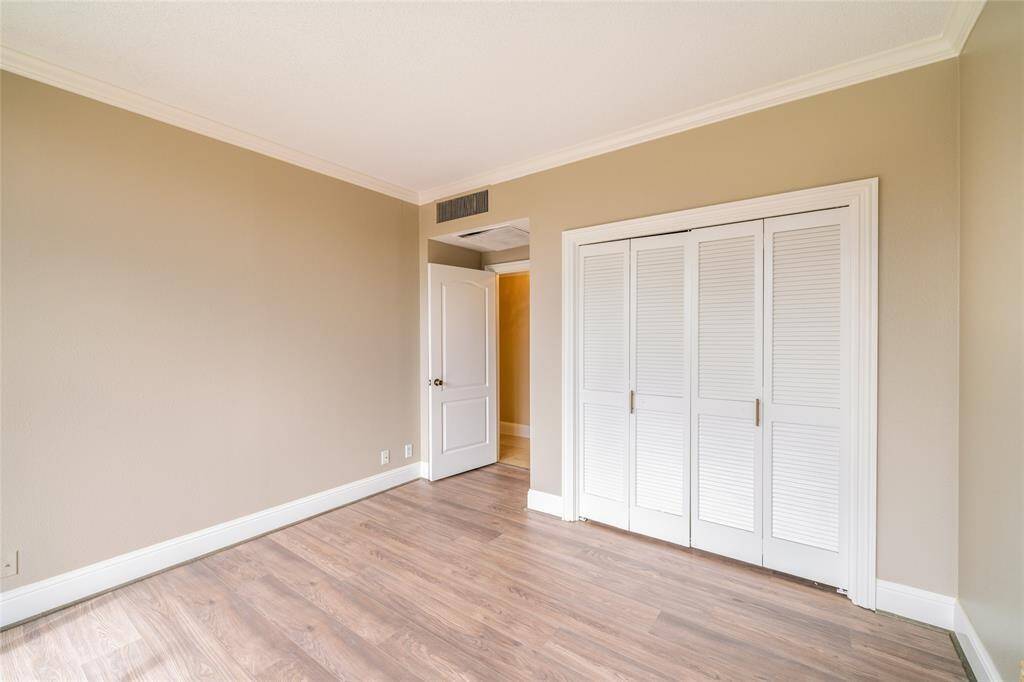 This room features warm beige walls, light wood flooring, and white trim. It includes a white double-door closet and a doorway leading to another area. The space is well-lit and offers a clean, modern aesthetic.