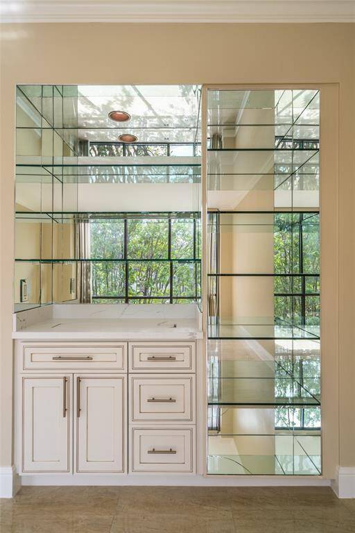 This elegant space features a built-in wet bar with mirrored shelving, offering ample storage and display options. The large window provides abundant natural light and a scenic view, enhancing the room's open feel.