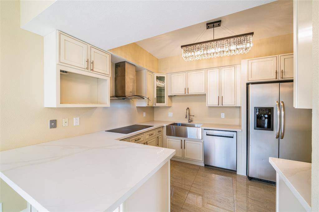 This modern kitchen features sleek stainless steel appliances, elegant cabinetry, a farmhouse sink, and a stylish chandelier. The open layout and ample counter space enhance functionality and appeal.