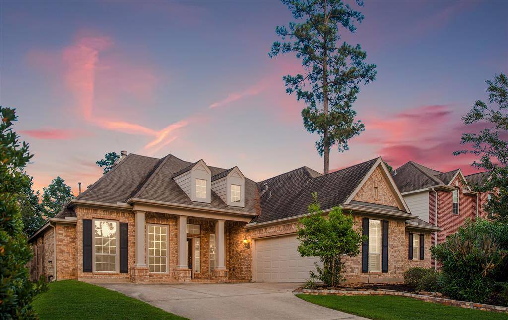 Step inside this charming, single-story brick home with a spacious driveway, well-maintained front yard, and mature trees. The house is illuminated warmly against a picturesque sunset sky.