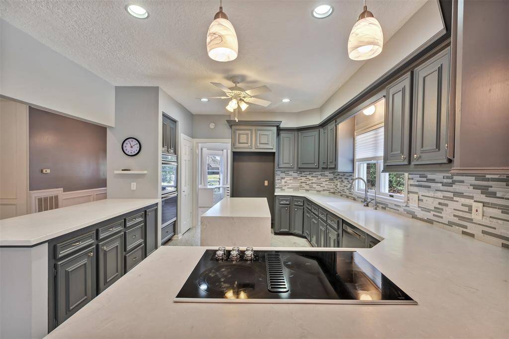 How gorgeous is this kitchen?  Recently updated with white/gray solid surface countertops, glass tile backsplash, and accented with darker grey cabinets!