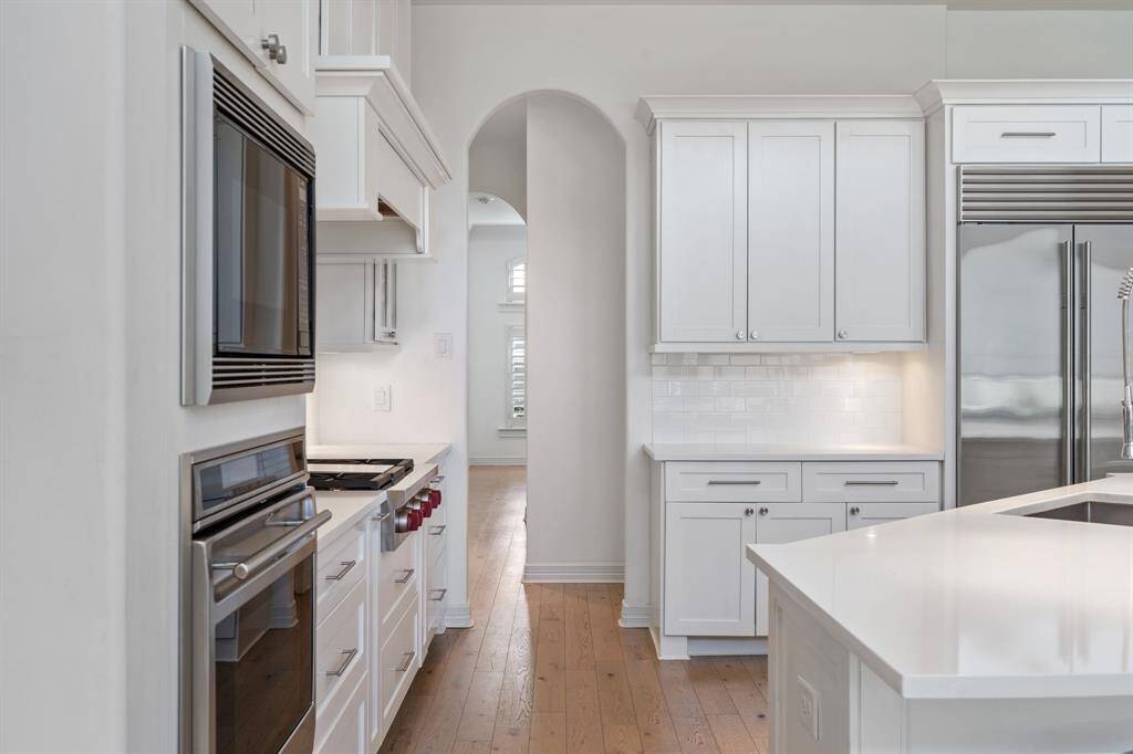 A modern, bright kitchen featuring sleek white cabinetry, stainless steel appliances, and a spacious island. The room has a clean, open feel with light wood flooring and ample natural light.