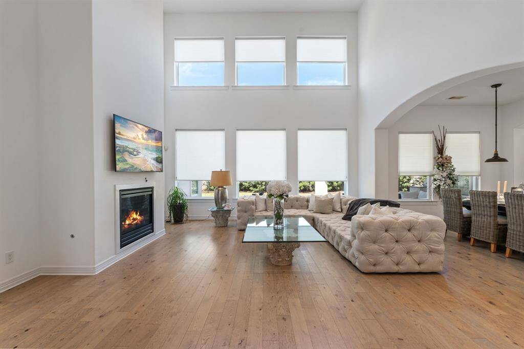 This open living room features high ceilings and large windows, allowing ample natural light. It includes a cozy fireplace, modern decor, and an adjacent dining area.