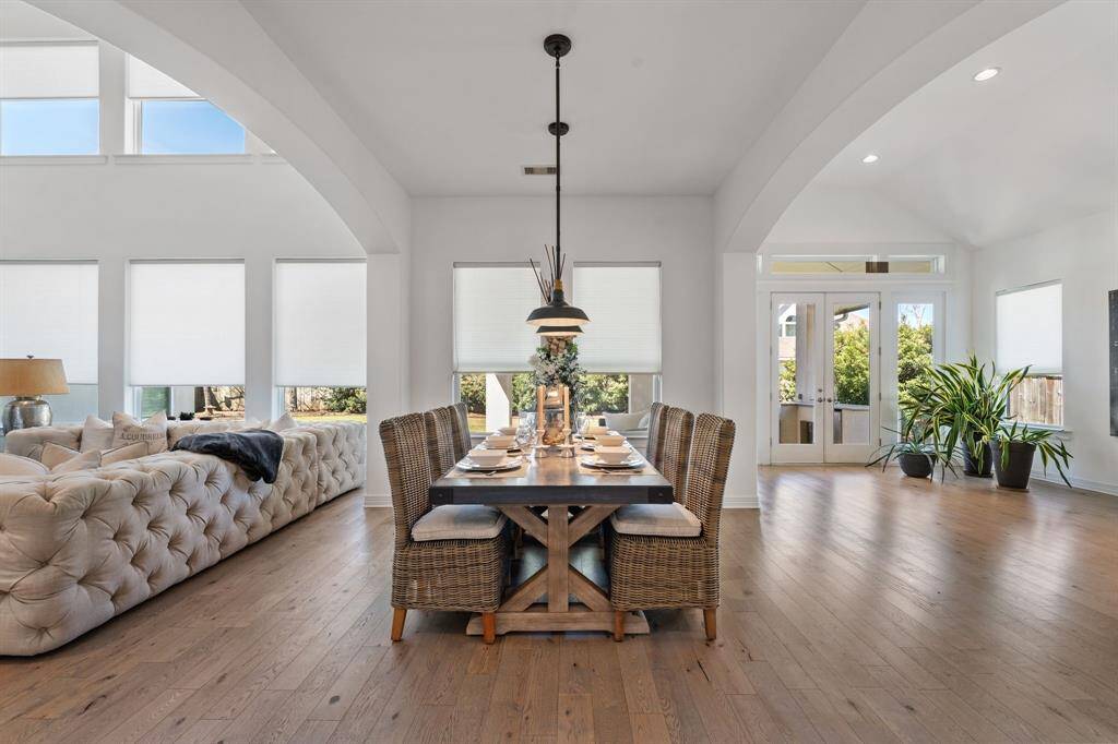 This spacious, light-filled open-concept room has large windows offering ample natural light. The French doors lead to a lush outdoor view.
