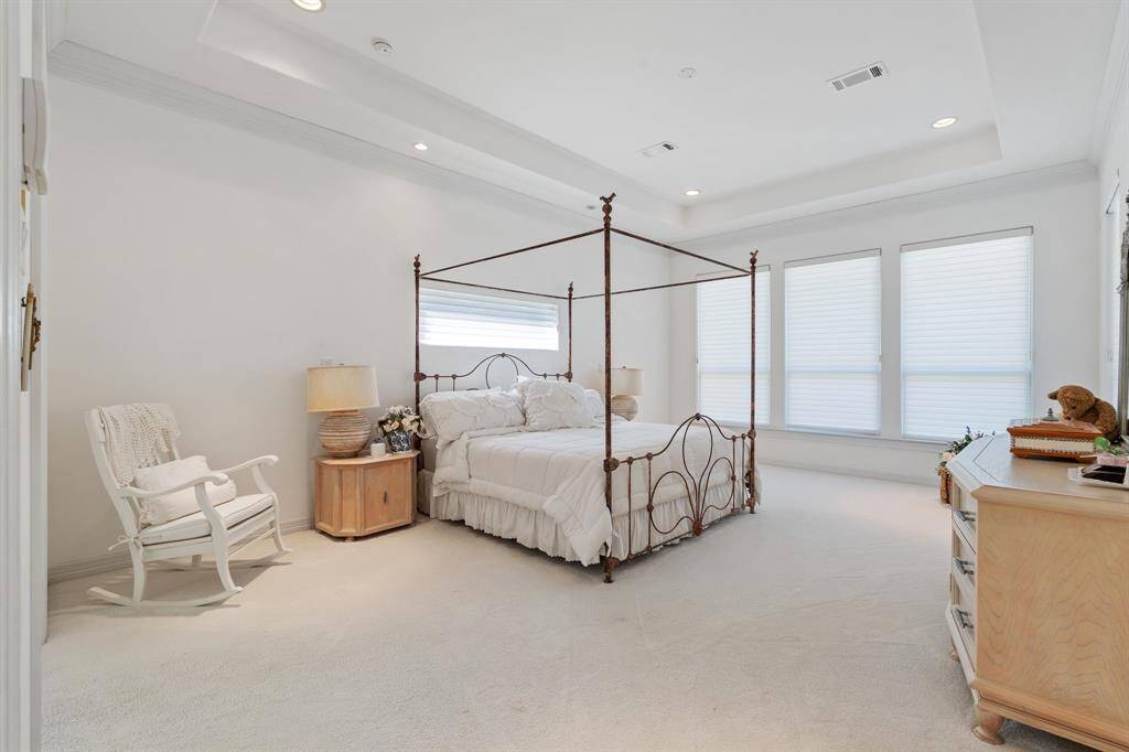 This spacious primary bedroom features a large room with neutral carpeting. There's abundant natural light from three tall windows.