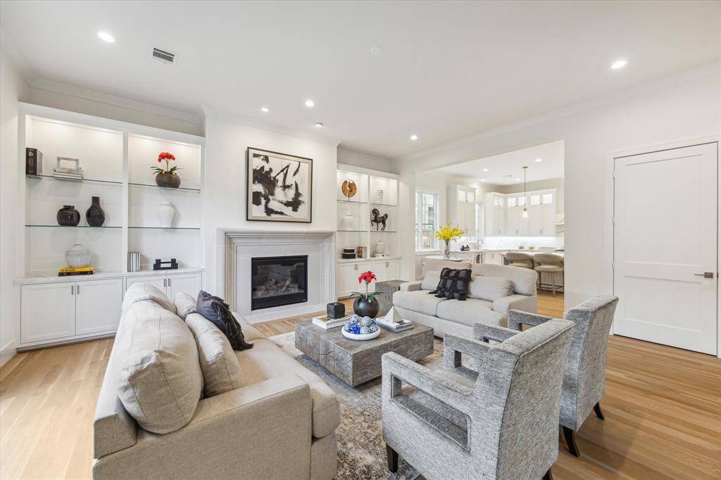 The the end of the Gallery is the Great Room featuring abundant light, wood floors, a gas jet Fireplace and abundant lighted, glass shelved etageres with cabinets below.