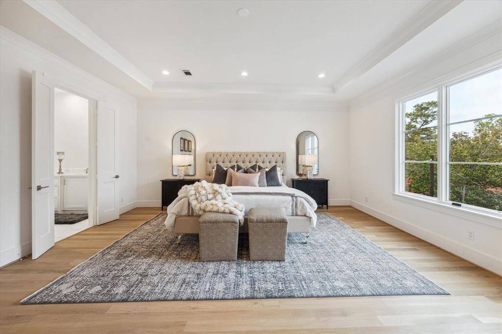 The Master Suite features wood floors, a tray ceiling outlined by thick crown moulding; through the broad casement windows is a Tanglewood treetop view.