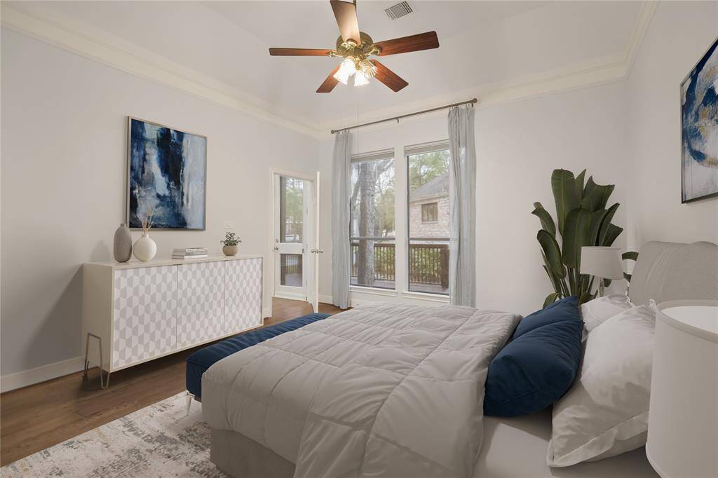 The serene and spacious primary bedroom on the first floor showcases beautiful wood floors, elegant crown molding, and windows offering stunning views of the back deck and the tranquil community lake. This picture shows the primary bedroom with virtual staging.