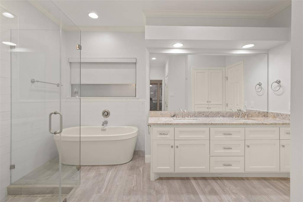 This updated primary bathroom exudes luxury, featuring a custom freestanding garden tub, a sleek glass-enclosed shower, and his-and-hers sinks with stunning granite countertops.