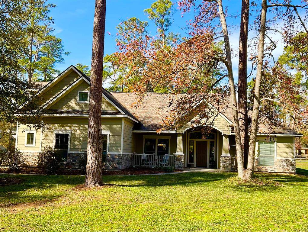Charming single-story home with a welcoming porch, nestled among mature trees. The exterior features a combination of stone and siding, offering a rustic yet modern appeal. The lush green lawn adds to the serene, natural setting.