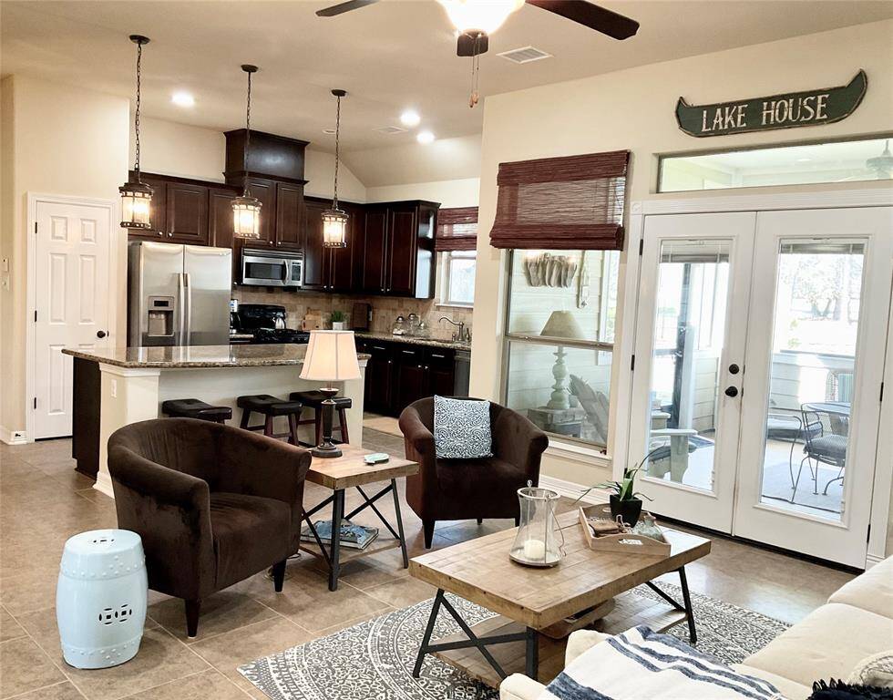 This inviting open-concept space features a modern kitchen with dark wood cabinets, stainless steel appliances, and a large island. The living area is cozy, natural light streams through glass doors leading to a screened in patio, creating a bright and airy atmosphere.