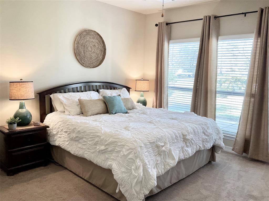 The primary bedroom features large windows with beige curtains, allowing plenty of natural light.