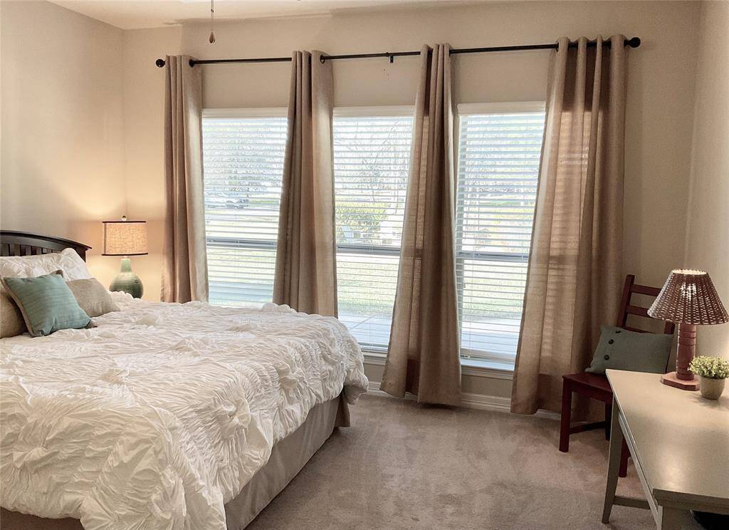 The primary bedroom features large windows with beige curtains, allowing plenty of natural light.