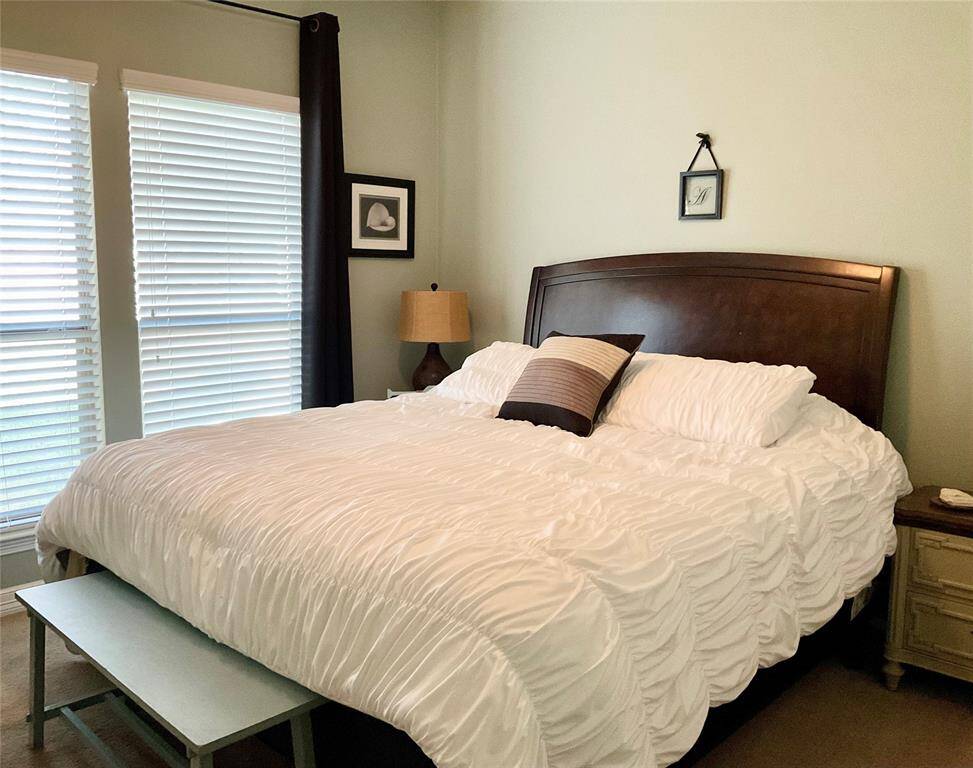 The secondary bedroom features a cozy setup, natural light streams in through the windows with blinds, completing the inviting atmosphere.