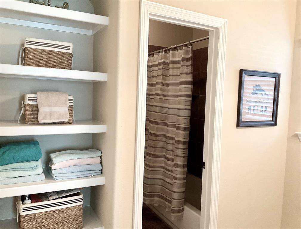 This bathroom features built-in shelving with storage baskets.  It includes a shower with a striped curtain and a framed picture on the wall, creating a cozy and organized space.