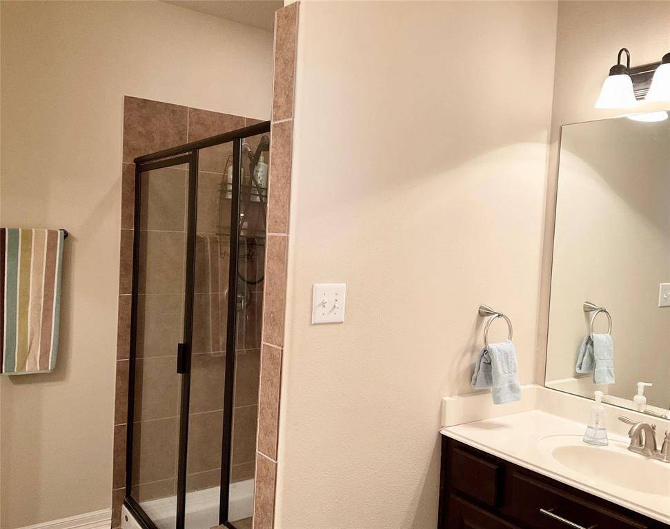 You will enjoy a modern bathroom with a glass-enclosed shower featuring tiled walls. There's a dark wood vanity with a white countertop, a large mirror, and simple lighting. The space is complemented by neutral wall colors.