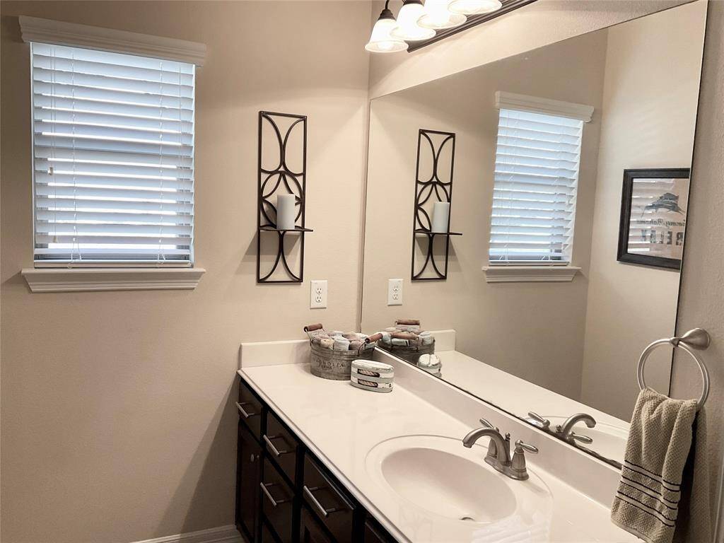 The bathroom features a modern design with a large mirror, elegant lighting, and a sleek vanity. Neutral tones create a calm and inviting atmosphere.